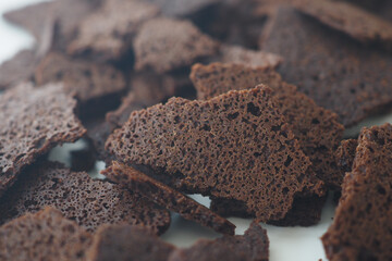 A Detailed CloseUp View of Crunchy Dark Brown Snack Pieces Displayed on a White Surface