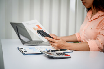 A close-up of a businesswoman working on a laptop in an office. As an accountant, she records...