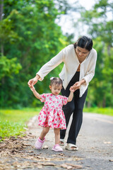 Naklejka premium A mother carries her little daughter through a green space surrounded by trees. They enjoy fresh air, outdoor fun, and quality time together, embracing nature on a beautiful sunny day