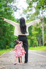 Obraz premium A mother carries her little daughter through a green space surrounded by trees. They enjoy fresh air, outdoor fun, and quality time together, embracing nature on a beautiful sunny day