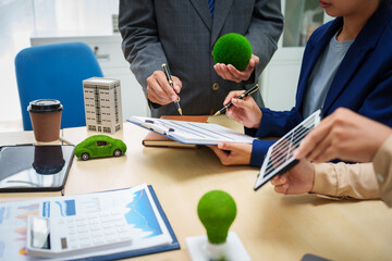 Asian business professionals in collaborate at desk with building models, planning sustainable...