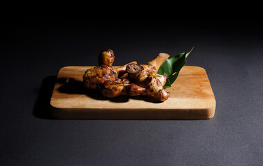 Fresh galangal root on wooden plate isolated on black background. Ingredients of herbs for healing and healthy food or medical concept.