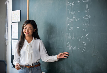 A woman is teaching a class about the human body. She is smiling and pointing to the board with the...