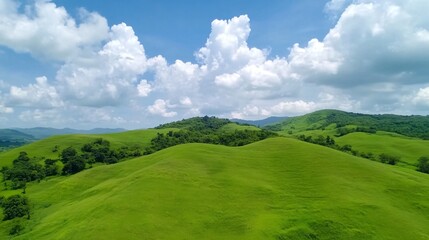 Obraz premium Lush green hills under a bright blue sky filled with fluffy clouds, showcasing a serene and picturesque natural landscape.