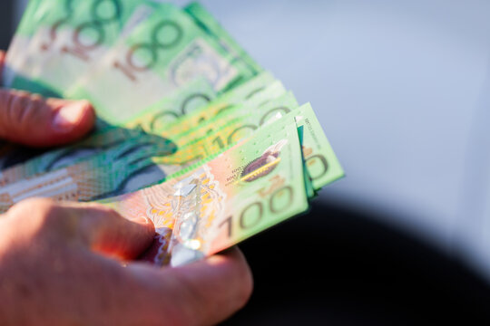 Middle aged mans hand holding one hundred dollar notes in Australian cash to pay for car