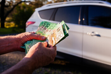 Middle aged mans hand holding one hundred dollar notes in Australian cash to pay for car