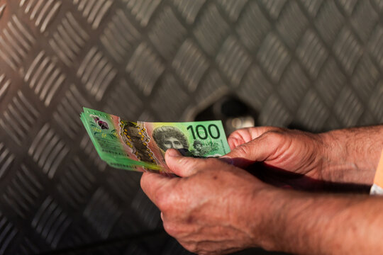 Middle aged man&rsquo;s hand holding hundreds of dollars of Australian cash beside meal texture