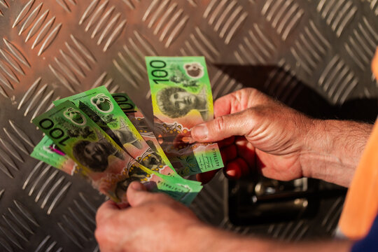 Middle aged man holding hundreds of dollars of Australian cash beside meal tool box on ute