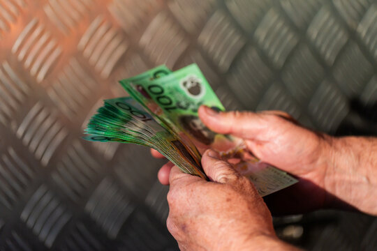 Middle aged man holding hundreds of dollars of Australian cash beside meal tool box on ute