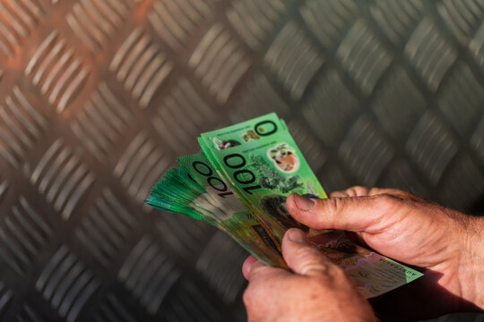 Middle aged man holding hundreds of dollars of Australian cash beside meal tool box on ute