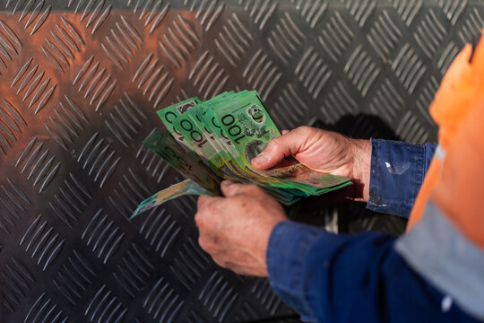 Middle aged man holding hundreds of dollars of Australian cash beside meal tool box on ute