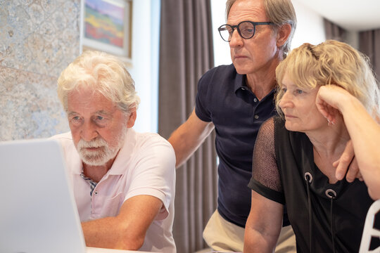 Concentrated couple of mature caucasian people learning how to use technology browsing on laptop with a senior expert man