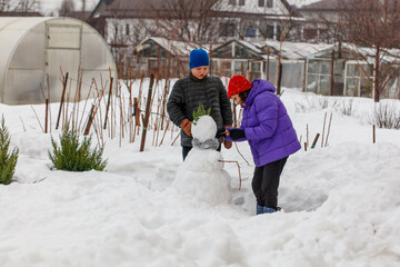 Two children are building a snowman in a snowy field