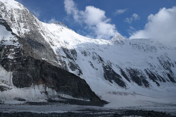 Obraz premium A stunning rock formation covered in snow, set against a clear blue sky with fluffy clouds in the background, creating a peaceful and breathtaking mountain landscape.