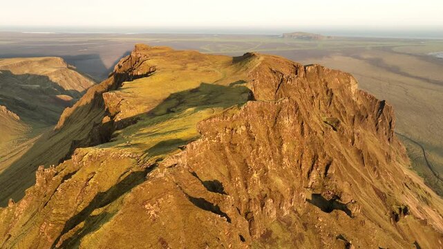 Aerial view of a rugged mountain ridge in Thakgil, Iceland, bathed in golden sunset light, with sprawling plains in the background.
