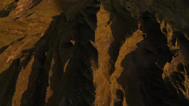 Aerial close-up of rugged hills in Thakgil, Iceland, with deep crevices illuminated by golden sunlight, highlighting the dramatic terrain.