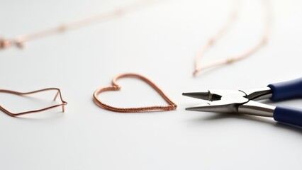 Pliers for jewelry making. Coiled copper wire forms a heart next to needle-nose pliers on a white surface, showcasing handcrafted jewelry creation.