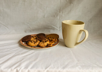 Chocolate chip cookies on a plate and a mug of coffee with a white background