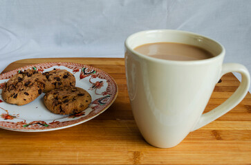 Chocolate chip cookies on a plate and a mug of coffee with a wooden background