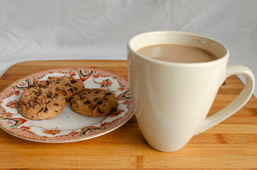 Chocolate chip cookies on a plate and a mug of coffee with a wooden background