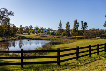 fenced off dam in green parkland beside housing suburb in Huntlee