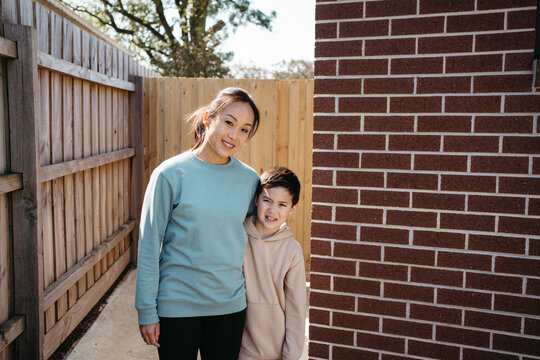 Mum and son standing outside in front of the brick wall of their house.