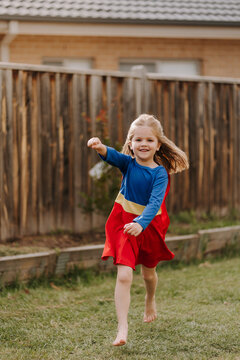 Happy little girl in a superhero costume running around backyard