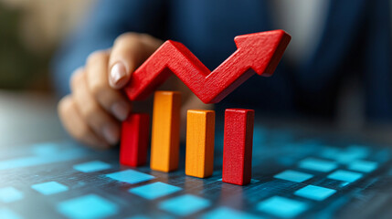 hand placing a red upward-trending arrow on top of a set of increasing bar graphs.  The graphs are red and orange,