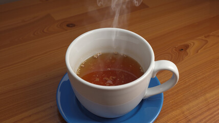 Steaming cup of tea on a wooden table in warm cozy lighting