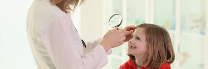 Optometrist examining little girl eye in doctor premise