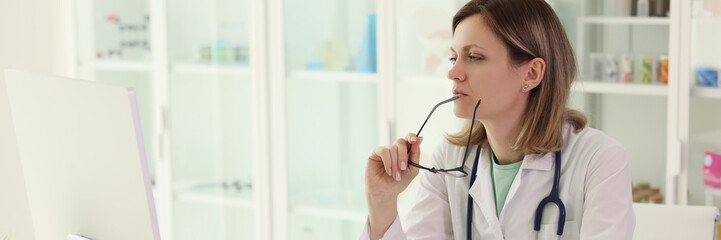Doctor holding glasses carefully examines data on computer