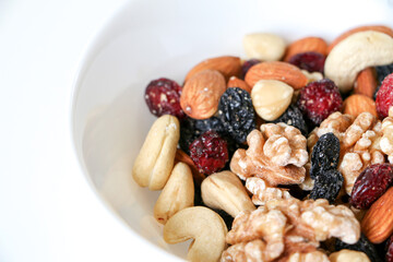 Healthy eating and living concept, close up of mixed nuts and dried fruits of almonds, walnuts, hazelnuts, cashew nuts, raisins and cranberries in a white bowl on right side of frame