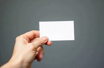 Fototapeta premium Female's hand holding blank business card on the grey background. Business card mockup