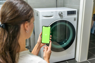 Young woman using mobile phone control via wi-fi and app for washing machine in home. Homesmart app, chroma key green screen