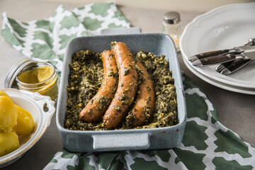 Oldenburger Grünkohl mit Pinkel Kohlwurst in Schale, Salzkartoffeln und Senf auf gedeckten grau Tisch mit grün Tuch, Teller, Besteck rustikal 
