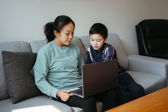 Mum working on her laptop on the couch with her kids.