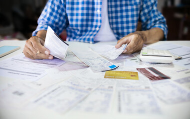 Asian man sitting at desk holding receipt of expenses and calculate all loan bills and try to find money to pay credit card debt, financial problem and inflation economy concept