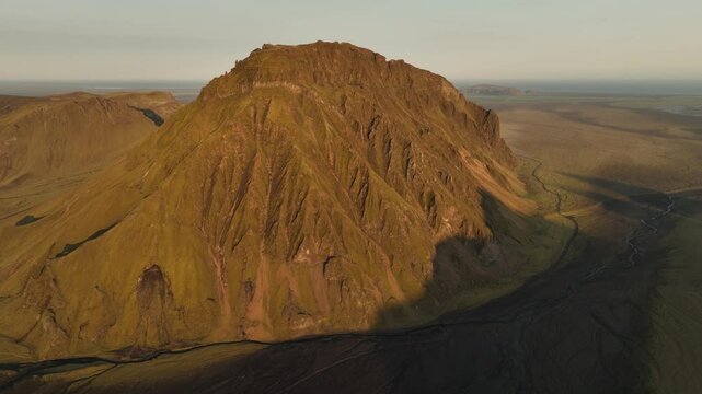 Aerial view of a prominent mountain in Thakgil, Iceland, illuminated by golden hour light, surrounded by vast plains and winding rivers.
