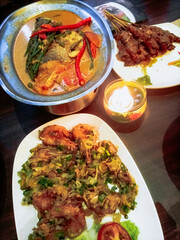 Flour fried shrimp, snapper head curry and chicken satay are served on wooden tables decorated with candlelight. Ready-to-eat cuisine concept.