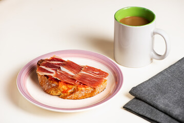 Serrano ham toast, olive oil and tomato with a cup of coffee with milk, a typical breakfast in Andalusia. White background.