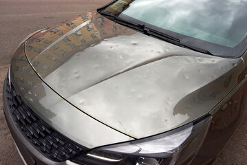 Parked car damaged by hail with visible dents on hood and cracks, need for auto repair and...