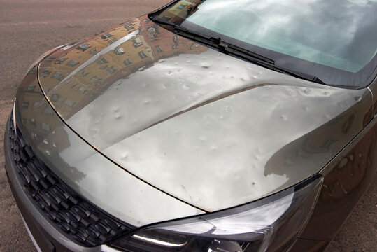 Parked car damaged by hail with visible dents on hood and cracks, need for auto repair and maintenance. Car body exterior with cosmetic damage, dents and severe impact from hailstorm
