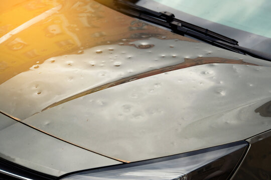Hail damaged car with visible dents on hood, exterior body with cosmetic damage with intact paint. Small dents in vehicle`s exterior, severe impact from hailstorm need for repair. Selective focus