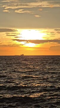 Verticle Sunset reflecting on the sea with waves and orange skies over the horizon at a serene beach