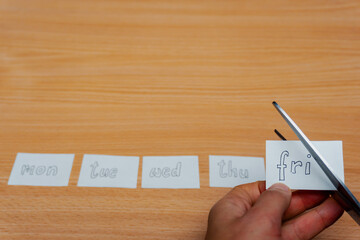 Five pieces of paper with the different days of the work week are layed on a wooden table. Friday is being cut off. 4-day work week concept. Changing working habits