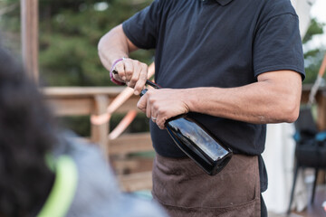 Man opening wine bottle wearing black t-shirt closeup of hands with corkscrew during outdoor gathering