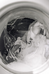 Close-up of a washing machine in action, with foam and bubbles during the wash cycle. Clean clothes, modern appliance, and everyday home life concept.