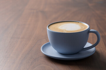 Fresh cappuccino in a blue cup on walnut table with copy space