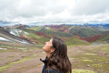 Beautiful young brunette Latina woman smiles with her eyes closed looking upwards recharging herself with the powerful energy of the beautiful colorful mountains of the Andes.