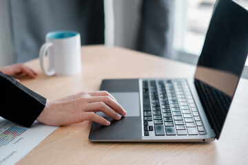 A business professional works on a laptop at a desk, accompanied by a coffee mug and document, in a modern office environment.